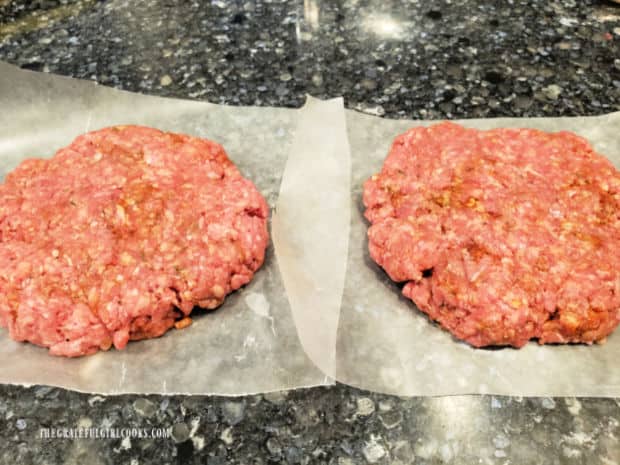 Two Cajun-seasoned burger patties on wax paper, before being cooked.