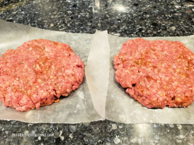 Two Cajun-seasoned burger patties on wax paper, before being cooked.