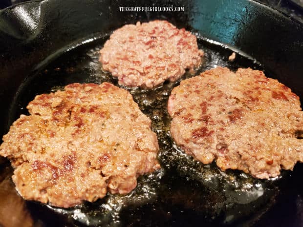 The Cajun-seasoned burger patties are flipped over to cook the other side.