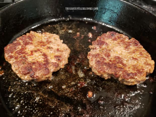 Two fully cooked Cajun-seasoned burger patties in a cast iron skillet.