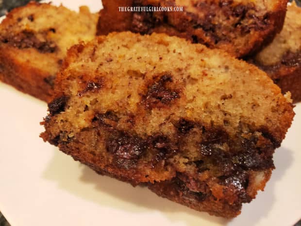 One slice of chocolate chip orange bread, on a white plate with more slices in the background.