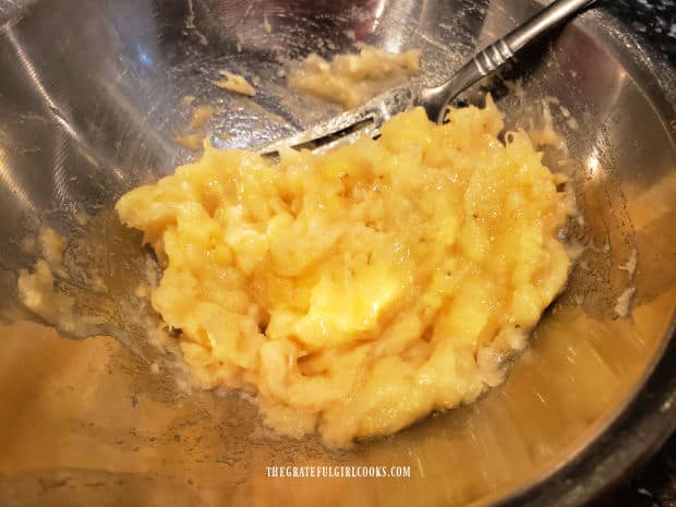 A banana is mashed with a fork in a small metal bowl.