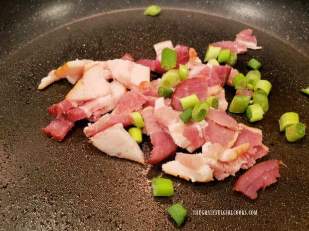 Bacon pieces and green onions are cooked in a large skillet.