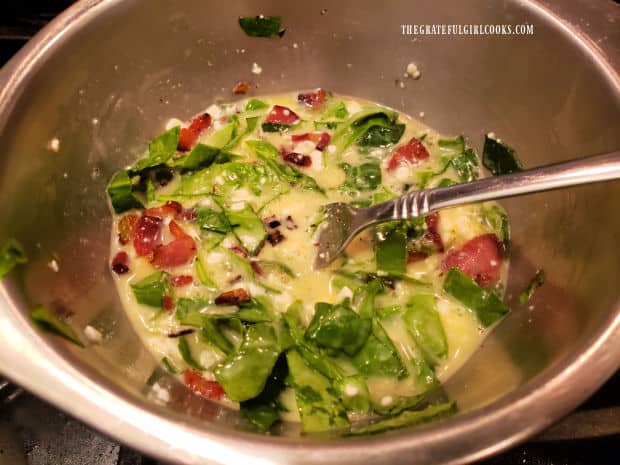 Cooked bacon and green onions are added to the egg mixture in silver bowl.