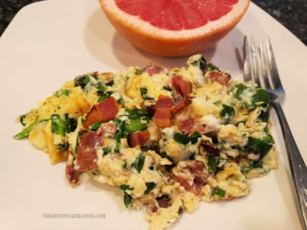 A white plate with a red grapefruit half and Florentine eggs and bacon on it.