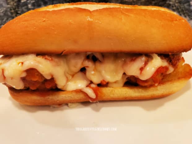 One of the Italian meatball sandwiches is served hot, on a white plate.