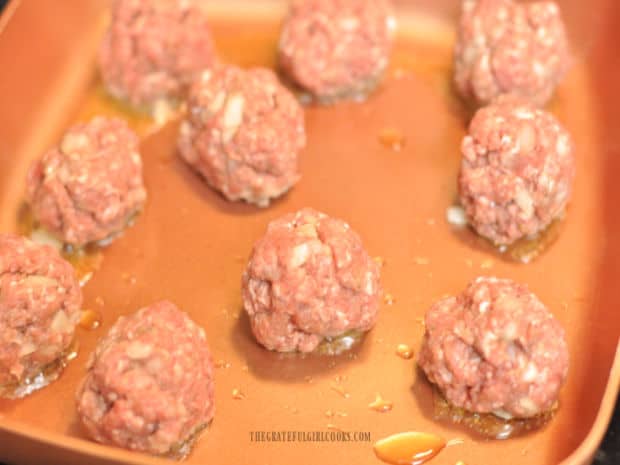 Italian meatballs cooking in hot oil in a skillet.