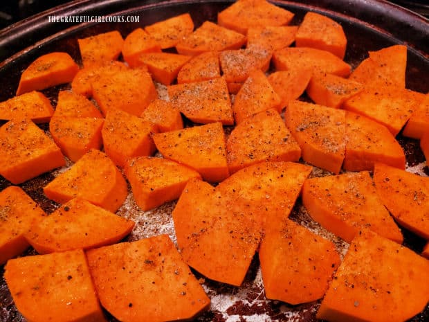 Seasoned sweet potato pieces are baked in a single layer on a greased baking sheet.