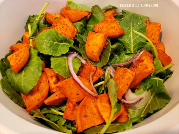 Kale leaves, red onion slices and roasted sweet potatoes are placed in salad bowl.