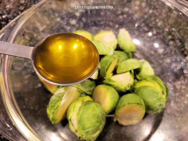 Olive oil is drizzled over the Brussel sprout halves in a mixing bowl.