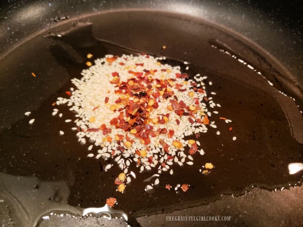 Red pepper flakes and white sesame seeds in oil in skillet.