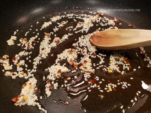 Sesame seeds, oil and red pepper flakes are stirred while cooking in skillet.