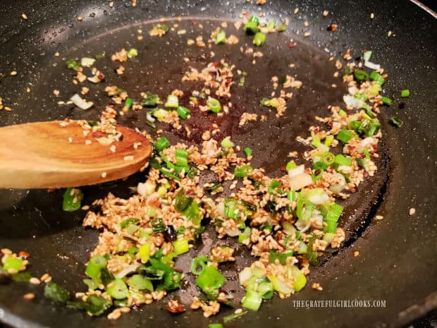 Minced garlic and green onions in skillet with toasted sesame seeds.