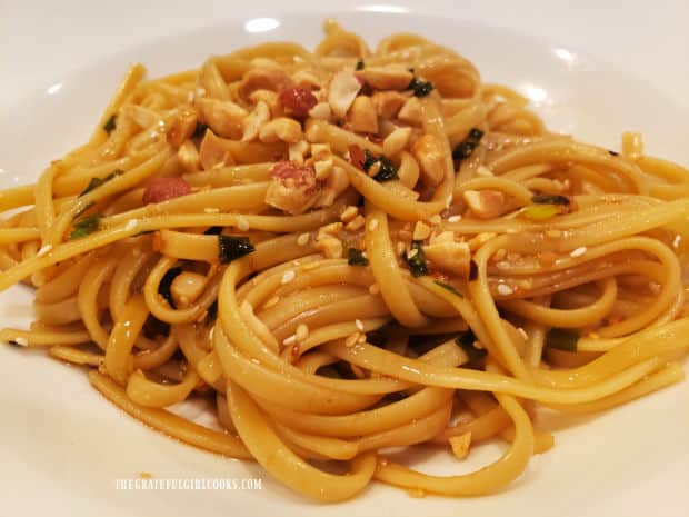 A white bowl of Asian sesame scallion noodles, with chopped peanuts on top.