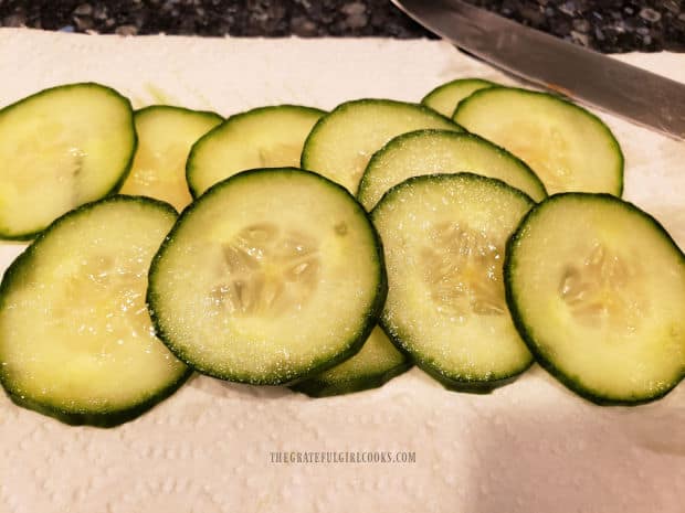 Thin slices of cucumber are cut and ready to be added to the sandwich.