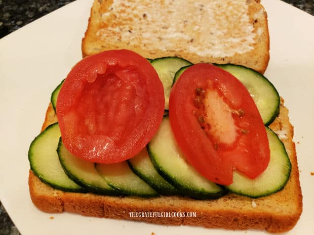 A couple small tomato slices are added on top of the sliced cucumbers.