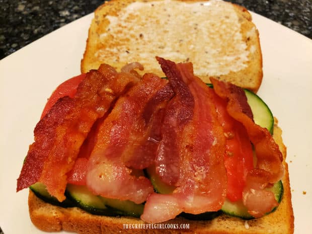 Cooked pieces of bacon are placed on top of the tomato slices on the sandwich.