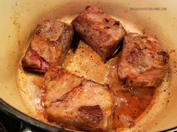 Browned on all sides, the four beef short ribs sit in a large Dutch oven.