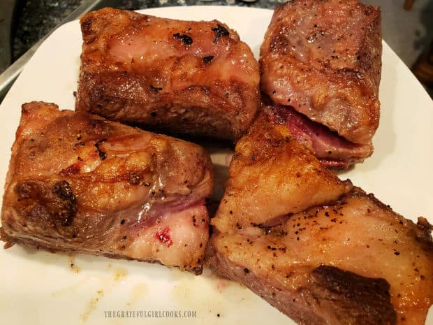 The four browned beef short ribs are removed from Dutch oven and rest on a plate.