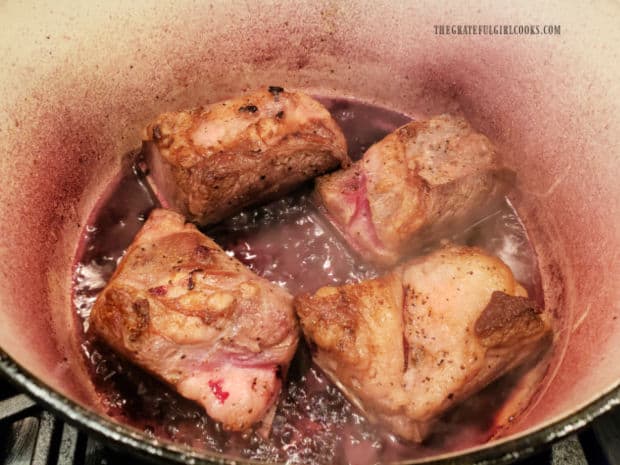Four browned beef short ribs are transferred back into pan with red wine reduction sauce.