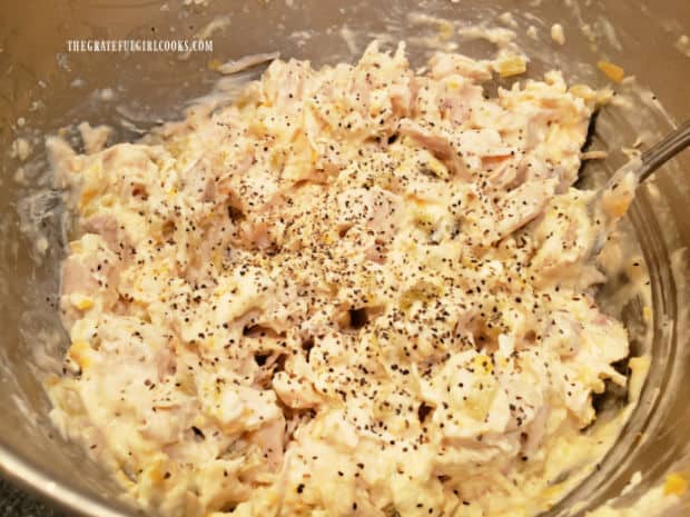 Seasonings are added to the chicken enchilada filling in a bowl.