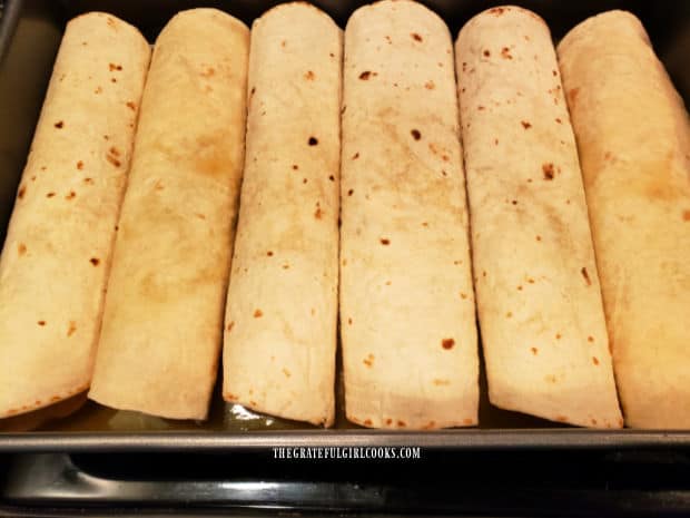 Filled enchiladas are placed in a baking dish for cooking.