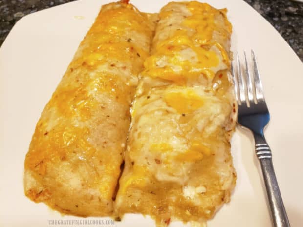 Two hot, baked chicken green chile enchiladas are served on a white plate.