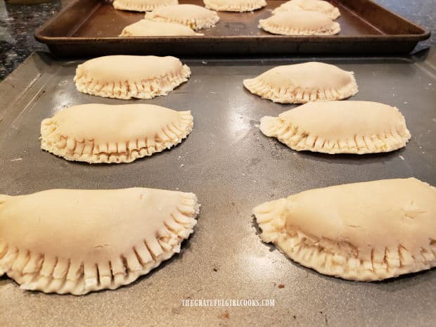 Hand pies are filled, sealed, and rest on baking sheets.