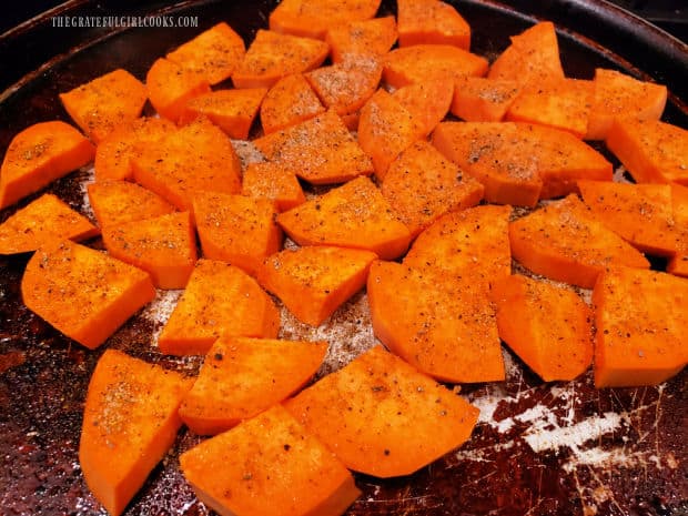 Sweet potato slices on pan are sprinkled with spice mix before baking.