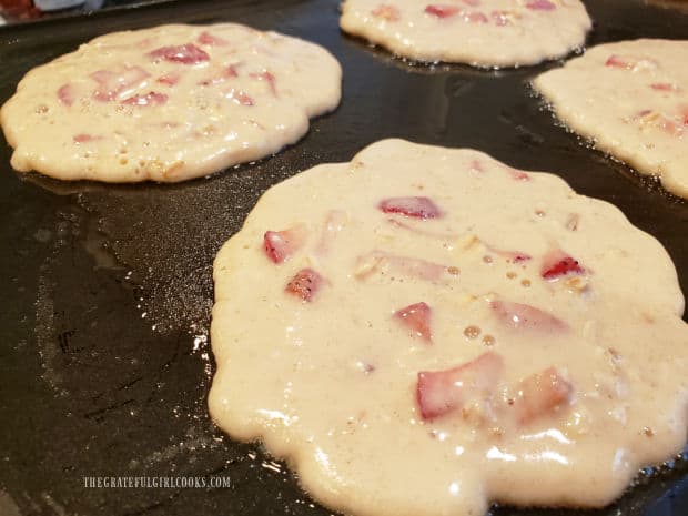 Strawberry oatmeal pancakes, cooking on a lightly oiled griddle.