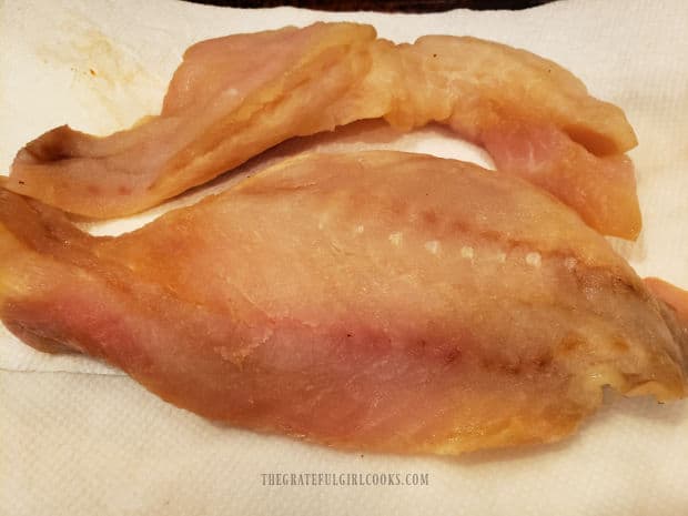 Two rockfish fillets are patted dry using paper towels.