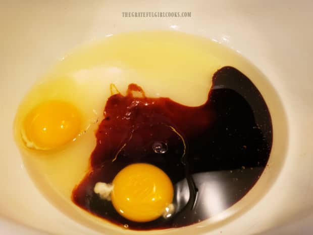Two eggs, molasses, sugar and vegetable oil, in a large white bowl.