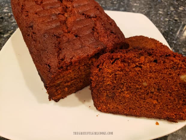 Carrot cinnamon nut bread loaf and one slice, on a white plate.