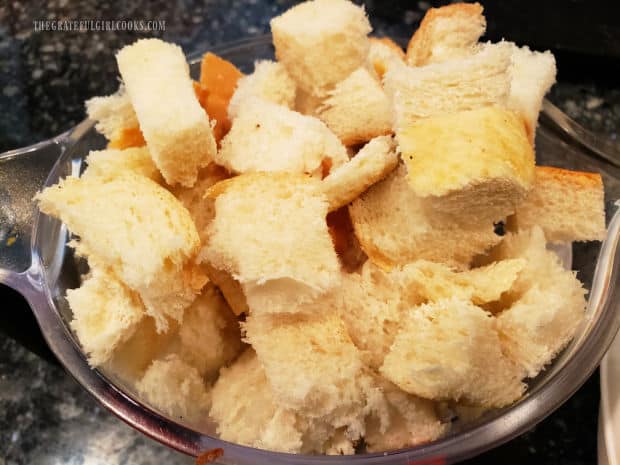 Day old bread cut into small, bite-sized cubes, in a measuring cup.