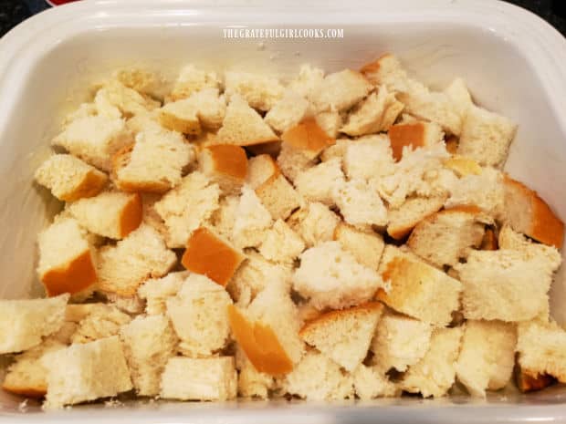 Cubed day old bread is spread in a buttered baking dish.