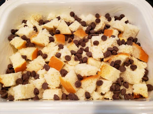 Chocolate chips sprinkled on top of the cubed bread in white baking dish.