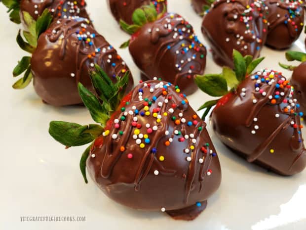 White plate with chocolate covered strawberries topped with colored sprinkles.