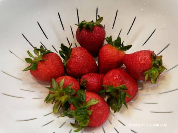 Strawberries in a colander are gently rinsed with water.