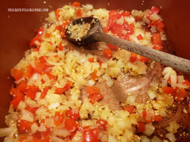 Onions, garlic and red bell peppers are cooked until tender in pan.