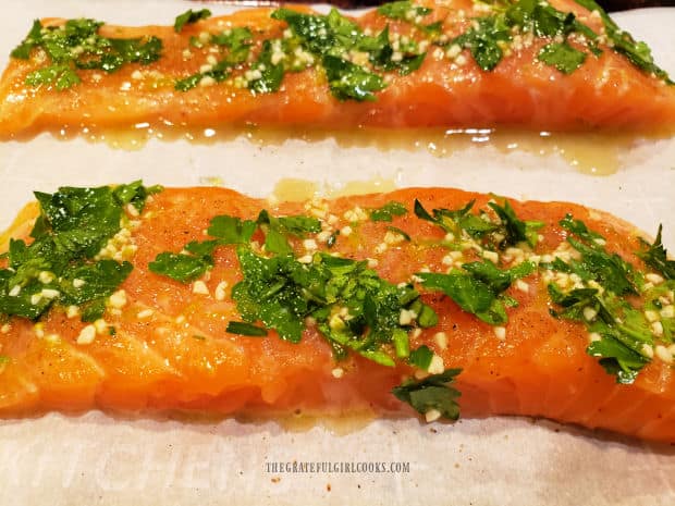 Garlic lime sauce is divided evenly on top of salmon fillets before baking.