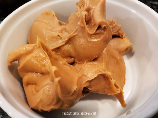 Creamy peanut butter in a small white bowl, ready to add to the cooked sauce.