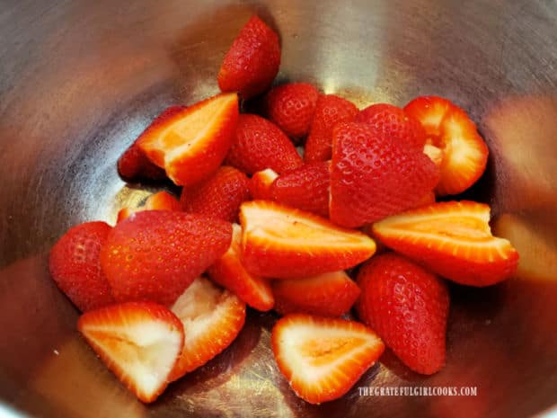 Strawberries are rinsed, cored, and sliced in half, then placed in bowl.