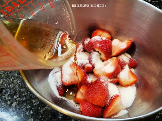 Pouring amaretto into the bowl with the strawberries and granulated sugar.