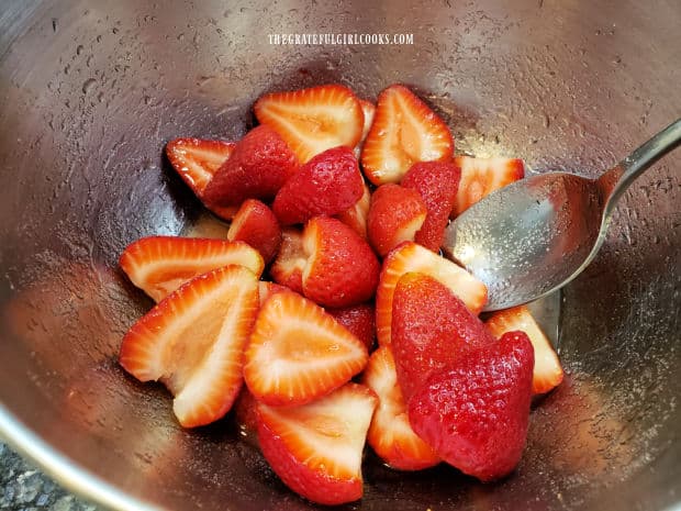 Strawberry halves are stirred, to dissolve sugar in the amaretto in bowl.