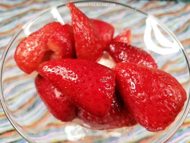 Macerated strawberries are added on top of the vanilla ice cream in dish.