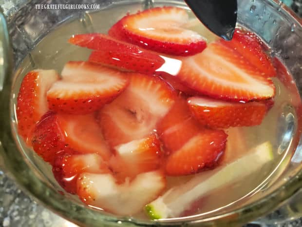 Sliced strawberries are added to the pitcher of water. 