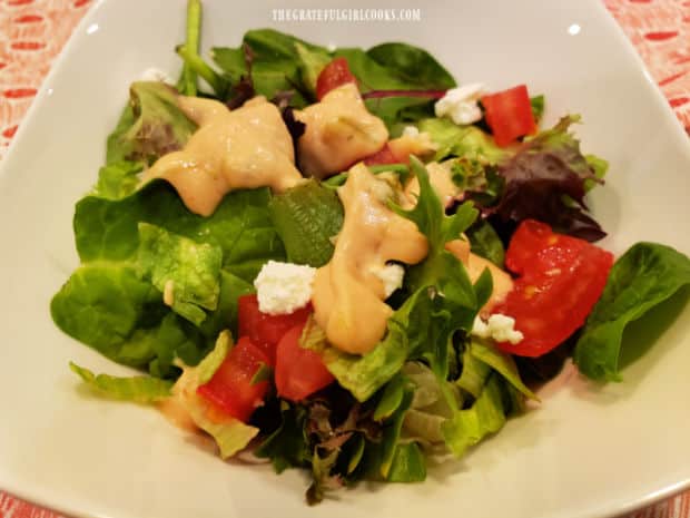 A white plate holding a green salad with thousand island salad dressing on top.