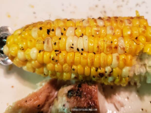 A piece of the lightly browned grilled corn on the cob, on a plate with chicken.