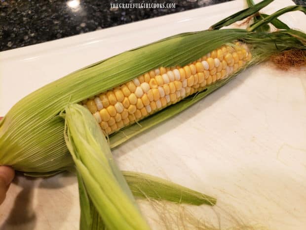 Husks are peeled back on corn, and the corn silks are removed.