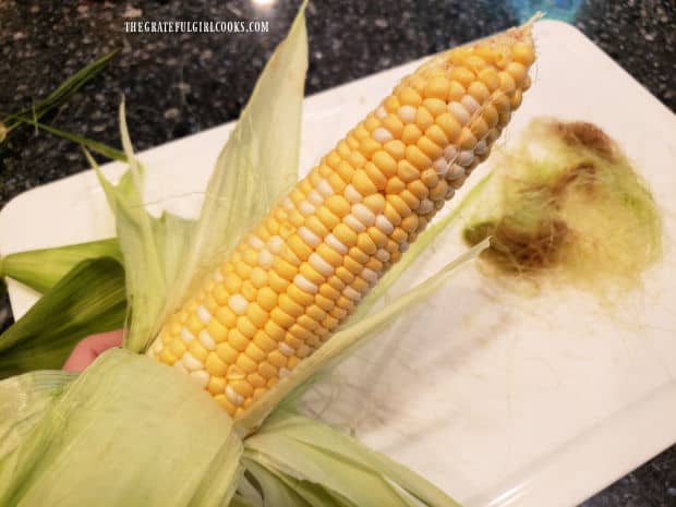 Corn husk is pulled back almost to the bottom, and corn silk is removed.